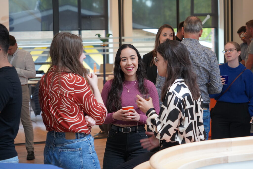 A group of three smiling women is chatting while holding beverages in their hands.